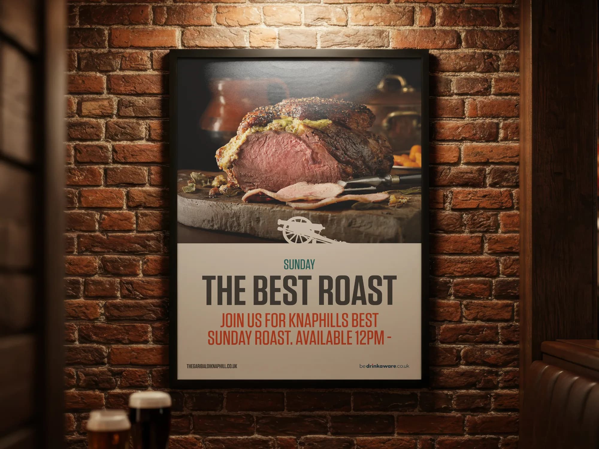 A framed Sunday roast poster on a brick wall beside a booth, two pints on the table