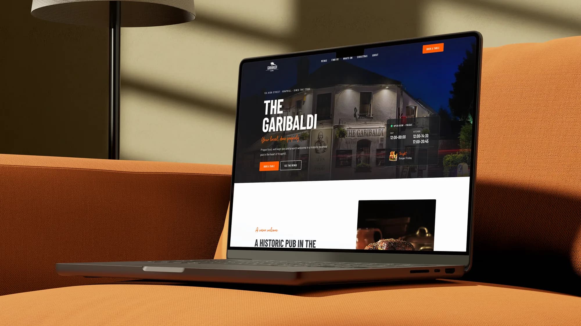 The Garibaldi homepage on a laptop on an orange sofa: the pub at night, with opening hours and tonight's event