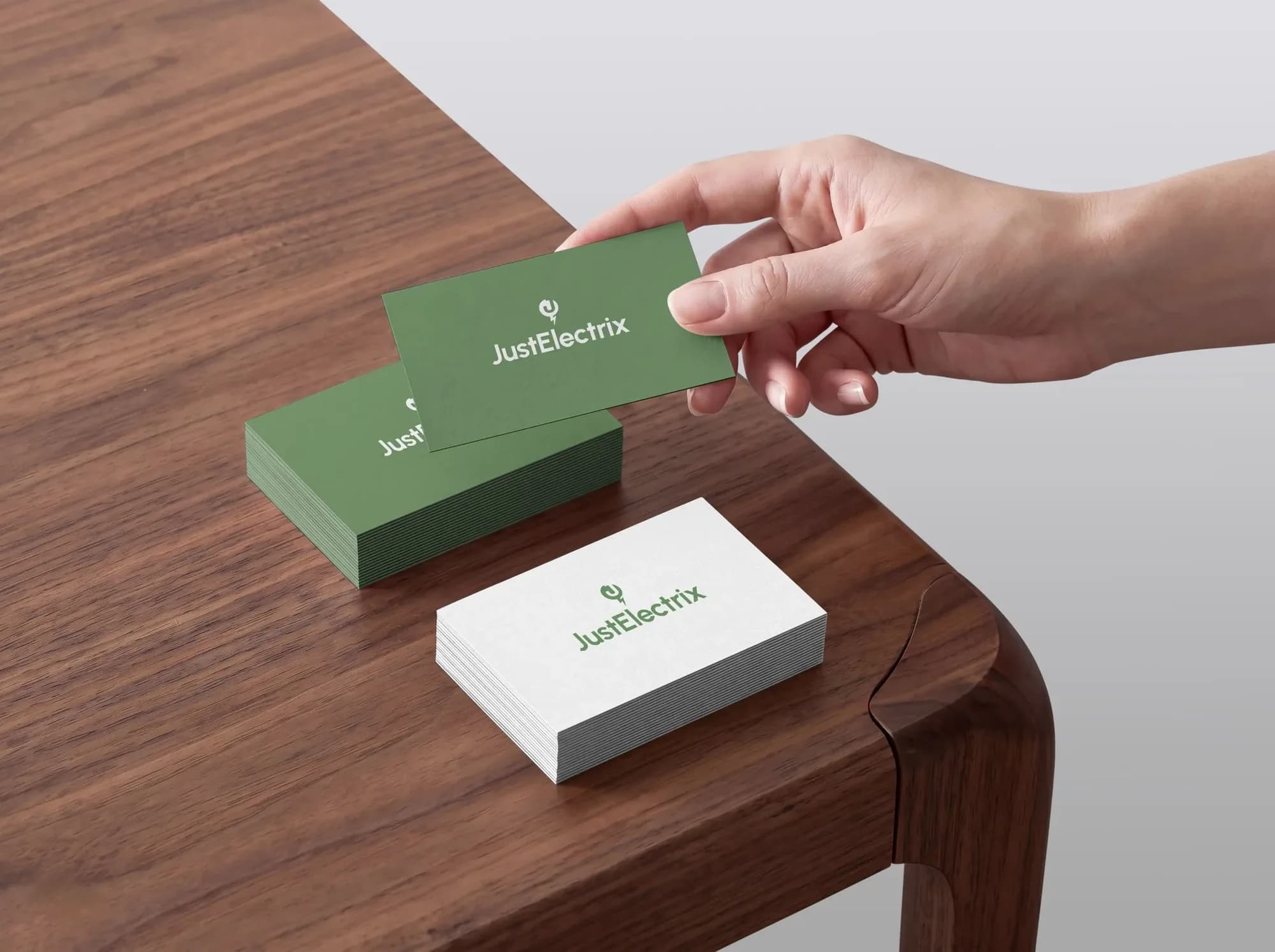 Green and white JustElectrix business cards on a walnut table