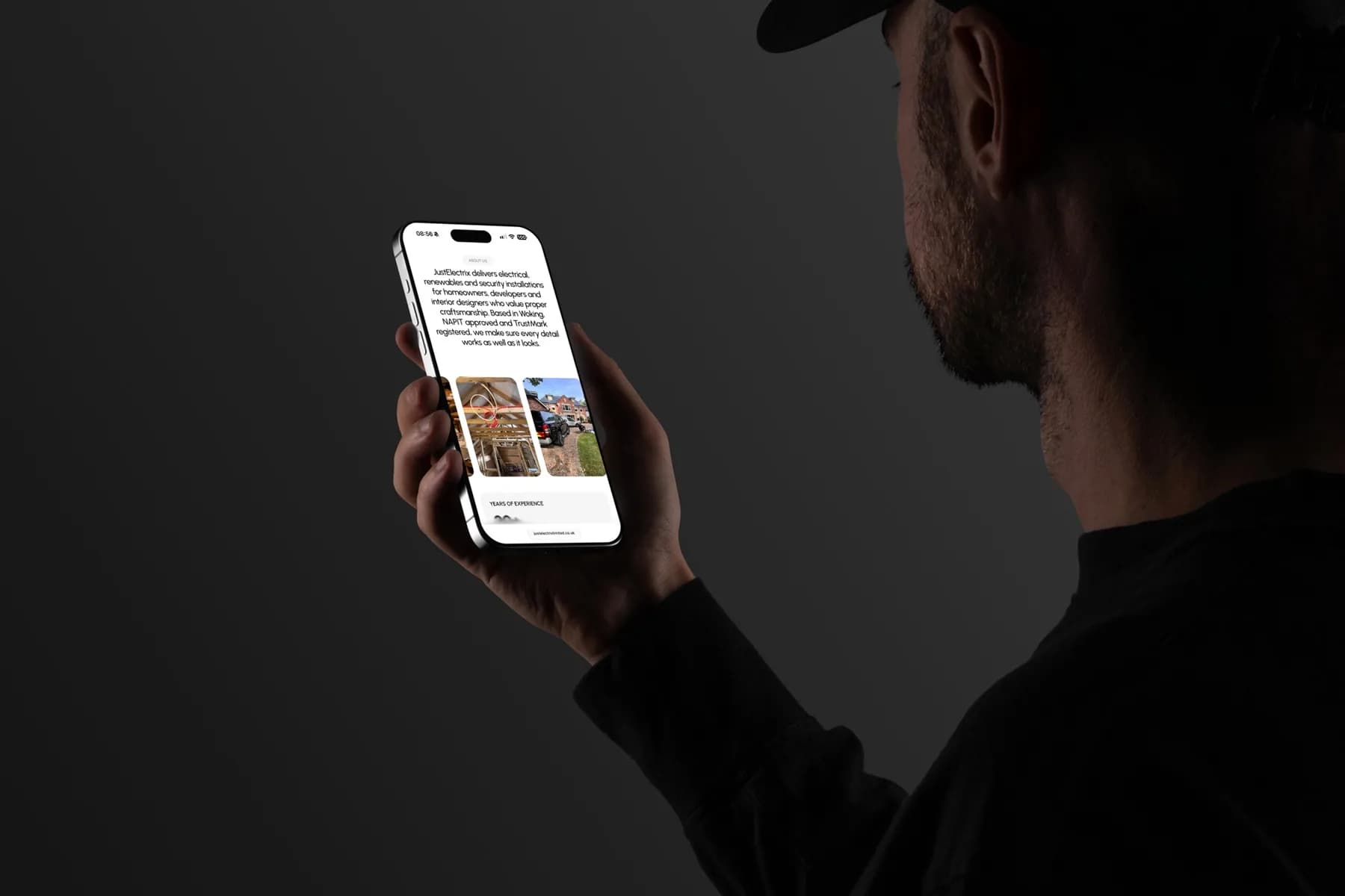 The JustElectrix website on a phone, held in a dark room