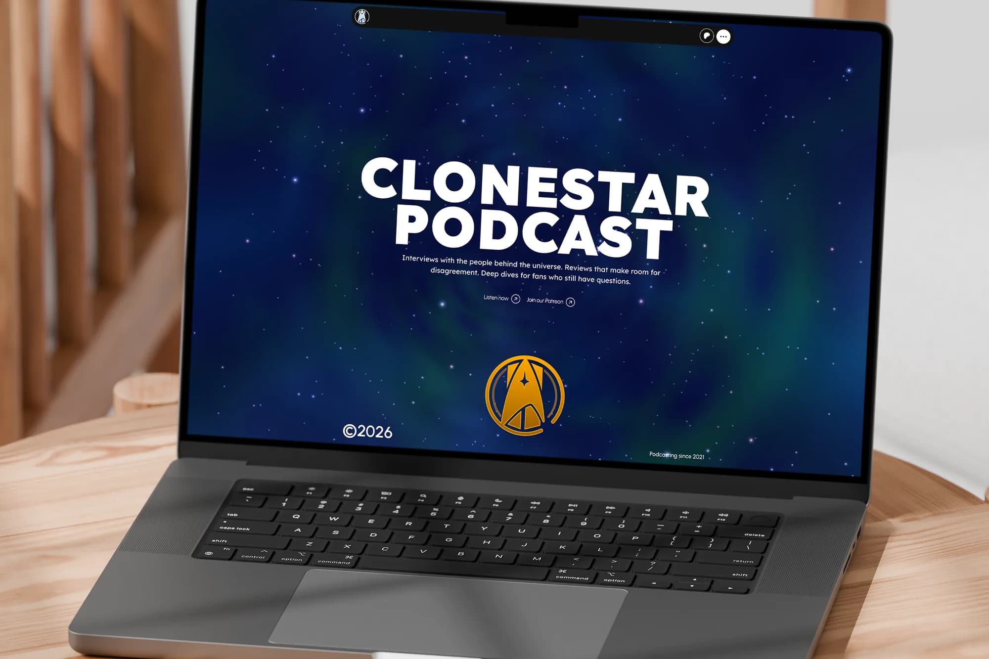 The Clonestar Podcast website on a MacBook, on a round oak table in a bright room