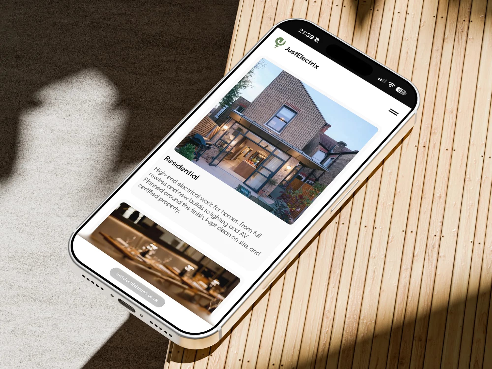 The JustElectrix residential page on an iPhone, lying on slatted oak in dappled sun