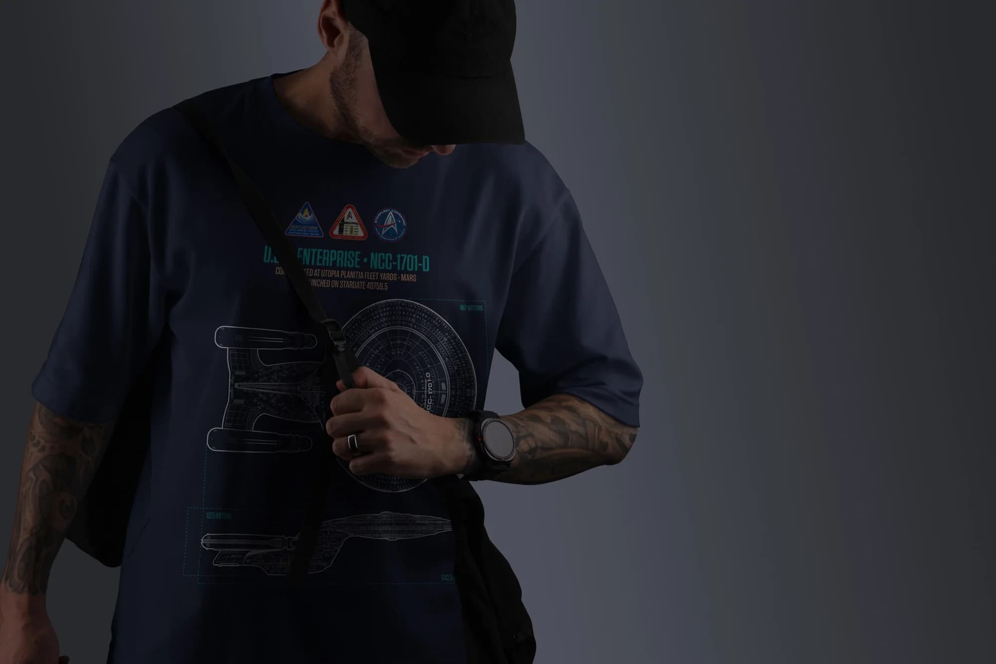 A navy T-shirt printed with a U.S.S. Enterprise NCC-1701-D schematic and mission patches